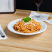 A Tuxton Sonoma bright white china soup bowl filled with spaghetti with parmesan cheese and parsley next to a glass of wine.