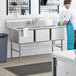 A man washing dishes in a commercial kitchen using a Regency three compartment sink.