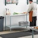 A man in an apron standing at a Regency stainless steel work table with undershelf.