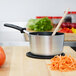 A Vollrath Wear-Ever sauce pan with a wooden spoon in a pot of carrots on a wooden surface.