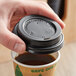 A hand putting a black lid on a cup of coffee.