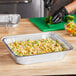 A person cutting vegetables in a Choice foil pan on a table.