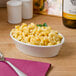 A Tuxton eggshell oval baker filled with macaroni and cheese on a table with wine.