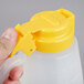 A person holding a Tablecraft yellow plastic dispenser jar with a yellow lid.