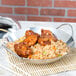 A Thunder Group stainless steel wok serving dish filled with rice and chicken on a table in an Asian cuisine restaurant.