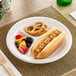 A Dart white foam plate with a hot dog, mustard, and other food on it.