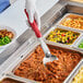 A person using a Vollrath Jacob's Pride heavy-duty perforated basting spoon with a red handle to serve food.