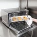 A hand holding a tray of cookies in a Waring countertop convection oven.