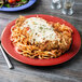 A red Cranberry Diamond Harvest plate with cheese and pasta on a table.