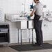 A man using a Regency stainless steel two compartment sink in a professional kitchen.