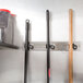 A T&S stainless steel mop hanger on a wall holding a mop and brooms.