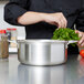 A chef in a black shirt uses a Vollrath stainless steel sauce pot to cook green vegetables.