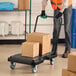 A black ergonomic platform truck with an adjustable handle, carrying two cardboard boxes.