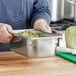 A person in a chef's uniform holding a Vollrath stainless steel container of lettuce.