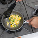 A hand using a spatula to cook scrambled eggs and peppers in a Vollrath Wear-Ever non-stick fry pan on a stove.