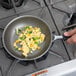 A hand using a Vollrath Wear-Ever aluminum non-stick frying pan to cook scrambled eggs with green peppers.