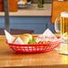 A Tablecraft red jumbo oval polypropylene fast food basket on a table with a sandwich and beer.