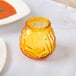 A yellow glass vase with a Sterno Amber Venetian Candle inside on a table.