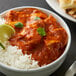 A bowl of chicken curry with rice and lime wedges on a black surface.