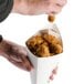A person holding an American Metalcraft cardboard square fry cone filled with fried chicken.