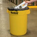 A person holding a yellow Continental 32 gallon trash can.