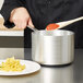 A chef stirring red sauce in a Vollrath Wear-Ever saucepan.