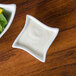 A bowl of salad and dressing in a white square bowl.