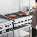 A woman cooking ribs on a Garland gas charbroiler with adjustable grates.