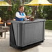 A man standing behind a Cambro portable bar with a drink.