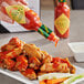 A hand pouring TABASCO Cayenne Garlic Pepper Hot Sauce onto a plate of chicken wings.
