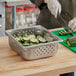 A person cutting cucumbers in a Vollrath stainless steel steam table pan.