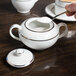 A person pouring sugar into a white 10 Strawberry Street porcelain sugar bowl.