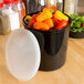 A black Cambro crock with lid on a table full of red and yellow peppers.