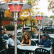 A group of people sitting at an outdoor patio table with a Schwank commercial patio heater.