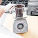 A hand in a white glove using a Taylor portion scale to weigh coffee beans in a plastic container.