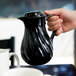 A hand holding a black Vollrath SwirlServe coffee server filled with a hot beverage.