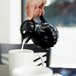 A person pouring coffee into a white mug from a black Vollrath SwirlServe beverage server.
