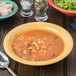 A Diamond Mardi Gras tropical yellow melamine bowl filled with soup and pasta on a table.