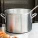 A silver Vollrath Wear-Ever sauce pot on a table with a wooden spoon inside.