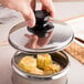 A hand holding a Town black lid over a silver container with food.