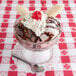 A Libbey Supreme Glass bowl filled with a banana split and chocolate sundae toppings with a spoon on a napkin.