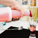 A person pouring a pink drink from a Carlisle Store 'N Pour container into a glass.