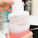 A person pouring red liquid from a Carlisle white plastic container with a red lid.