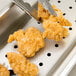 A pair of tongs holding fried chicken over a stainless steel tray with a Vollrath Super Pan V false bottom.