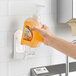 A hand using a Kutol Health Guard liquid soap dispenser to fill a wall-mounted dispenser.