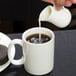 A person pouring milk from an American Metalcraft white porcelain bell creamer into a cup of coffee.