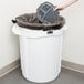 A hand holding a plastic container in a white Rubbermaid commercial trash can.