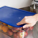 A hand holding a blue Carlisle Smart Lid on a container of apples.