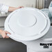 A woman holding a white lid on top of a trash can.