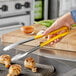 A person using Vollrath Jacob's Pride tongs to hold food over a grill.